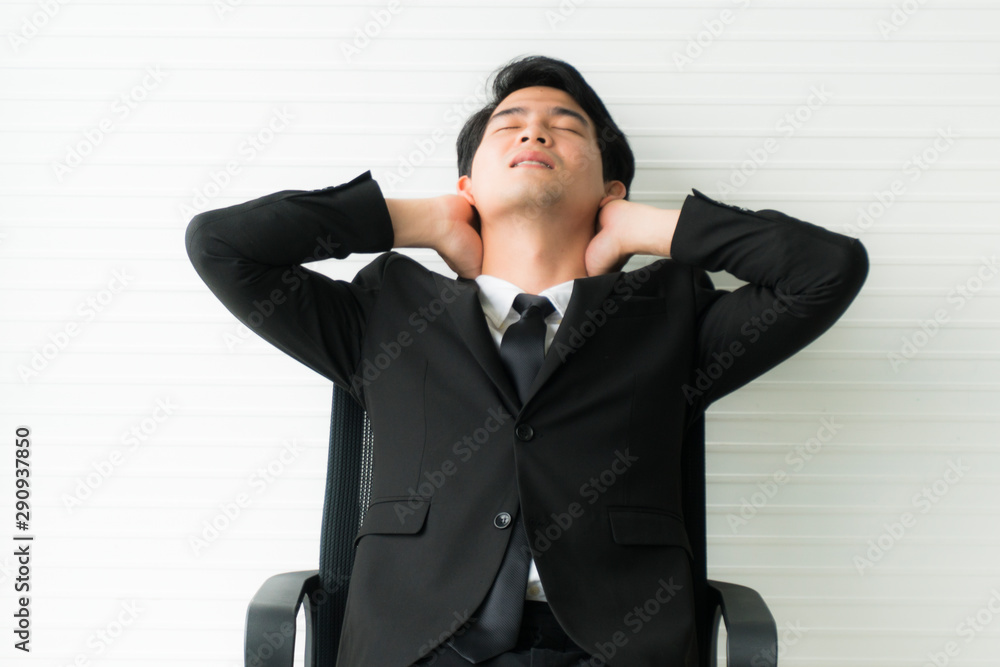 Young Asian handsome businessman wearing black suit arms behind head relaxing in his chair at office Young Asian handsome businessman wearing black suit arms behind head relaxing in his chair at office
