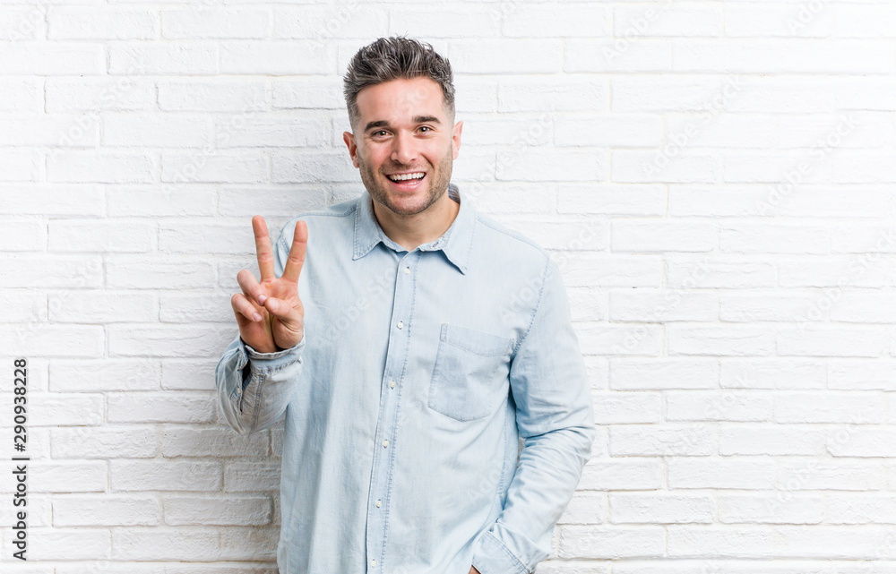 Young handsome man against a bricks wall showing victory sign and smiling broadly. Young handsome man against a bricks wall showing victory sign and smiling broadly.