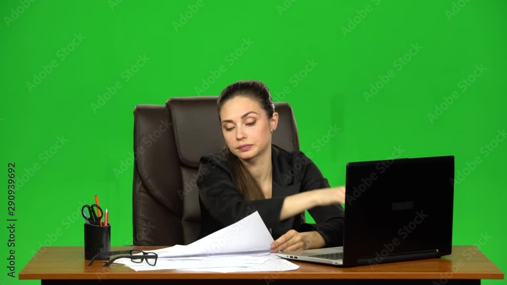 Tired woman reads document comparing information with a laptop, and crumples paper. Green screen Tired woman reads document comparing information with a laptop, and crumples paper. Green screen