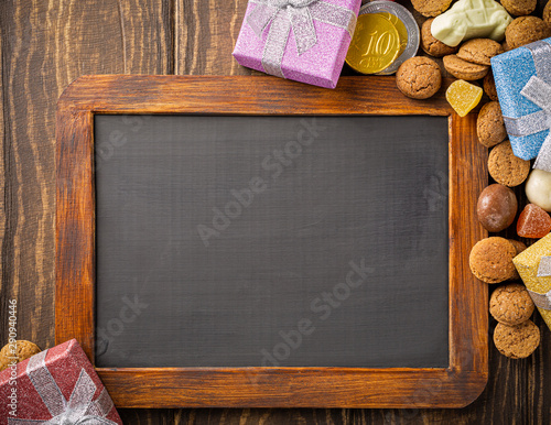 Dutch holiday Sinterklaas background with black chalkboard, gifts, pepernoten, traditional sweets strooigoed and carrots for Santa's horse. Flat lay and copy space. photo