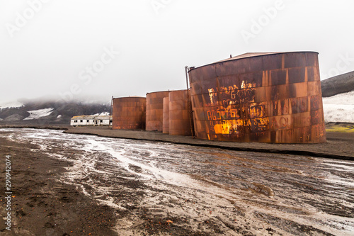Abandoned norwegian whale hunter station rusty blubber tanks with muddy river in the foreground at Deception island, Antarctic