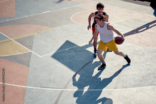 Top view of two young sporty men playing basketball on playground in morning .