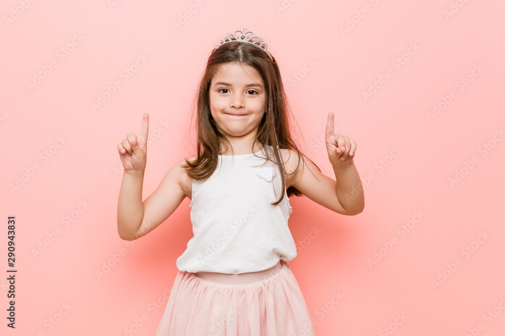 Little girl wearing a princess look indicates with both fore fingers up showing a blank space. Little girl wearing a princess look indicates with both fore fingers up showing a blank space.
