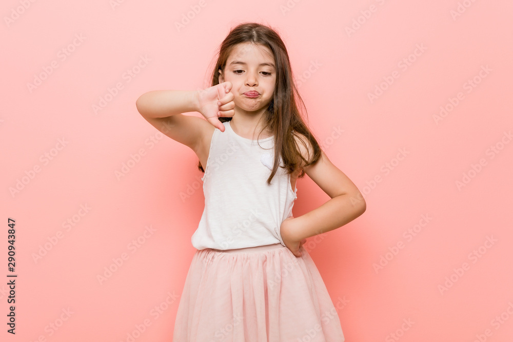 Little girl wearing a princess look showing a dislike gesture, thumbs down. Disagreement concept. Little girl wearing a princess look showing a dislike gesture, thumbs down. Disagreement concept.