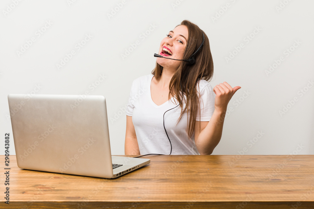Young telemarketer woman points with thumb finger away, laughing and carefree.