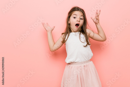Little girl wearing a princess look receiving a pleasant surprise, excited and raising hands.