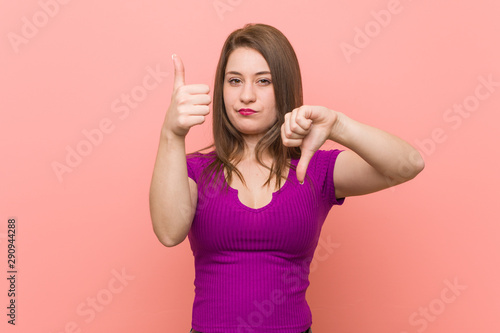 Young hispanic woman against a pink wall showing thumbs up and thumbs down, difficult choose concept