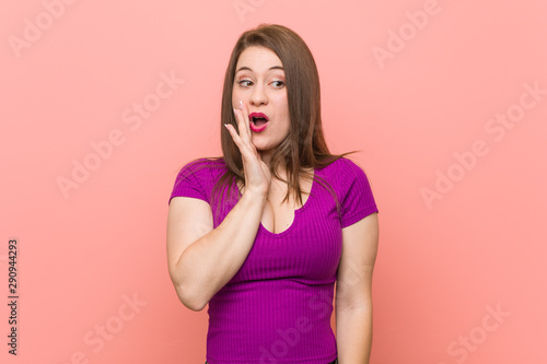 Young hispanic woman against a pink wall is saying a secret hot braking news and looking aside