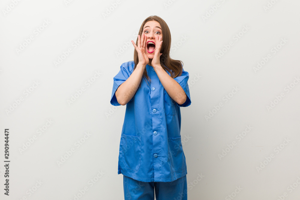 Young nurse woman against a white wall shouting excited to front. Young nurse woman against a white wall shouting excited to front.
