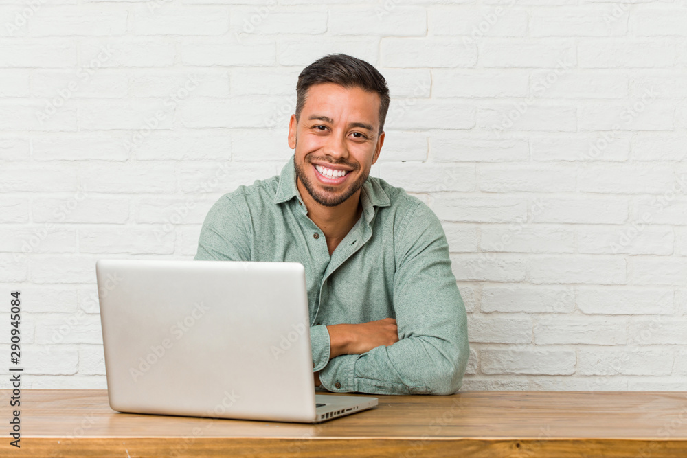 Young filipino man sitting working with his laptop laughing and having fun. Young filipino man sitting working with his laptop laughing and having fun.