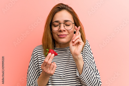 Young woman holding a strawberry crossing fingers for having luck photo