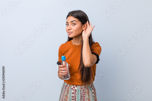 Young arab woman holding a water bottle trying to listening a gossip.