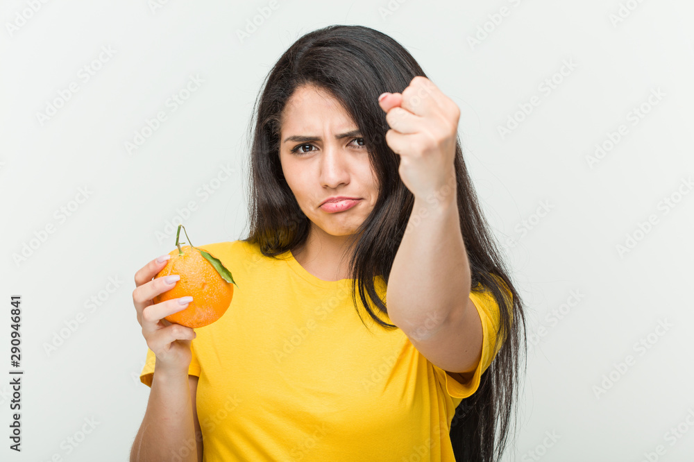 Young hispanic woman holding an orange showing fist to camera, aggressive facial expression. Young hispanic woman holding an orange showing fist to camera, aggressive facial expression.