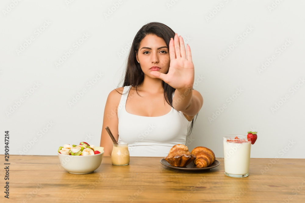 Young curvy woman taking a breakfast standing with outstretched hand showing stop sign, preventing you. Young curvy woman taking a breakfast standing with outstretched hand showing stop sign, preventing you.