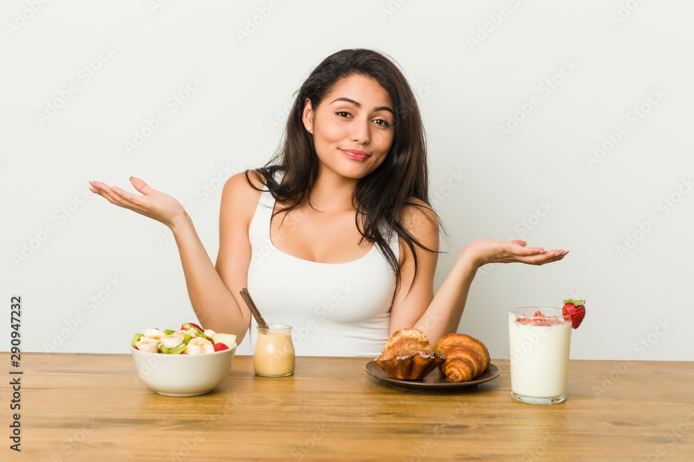 Young curvy woman taking a breakfast doubting and shrugging shoulders in questioning gesture. Young curvy woman taking a breakfast doubting and shrugging shoulders in questioning gesture.
