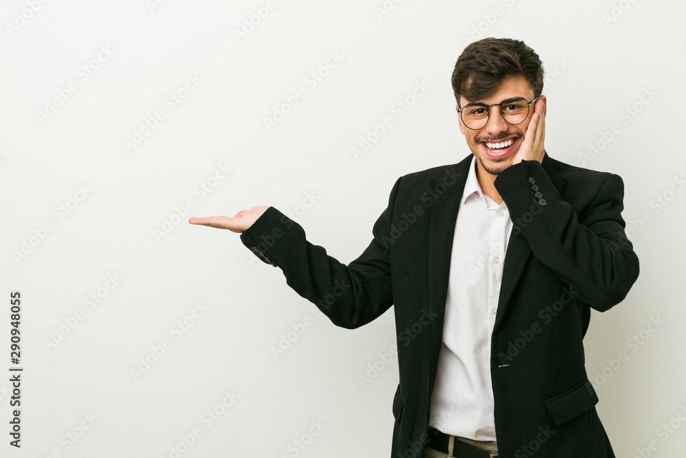 Young business hispanic man holds copy space on a palm, keep hand over cheek. Amazed and delighted. Young business hispanic man holds copy space on a palm, keep hand over cheek. Amazed and delighted.