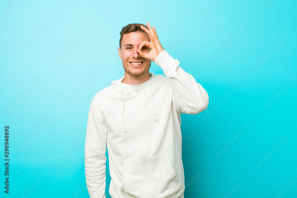Young caucasian sport man excited keeping ok gesture on eye. Young caucasian sport man excited keeping ok gesture on eye.
