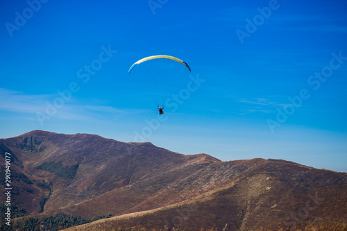 Paraglide silhouette flying over Carpathian peaks mountains on blue sky background. Feeling of freedom