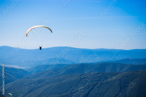 Paraglide silhouette flying over mountain peaks, beautiful rays of light in high mountain valley on background