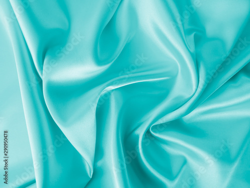 Smooth elegant wavy turquoise blue silk or satin luxury cloth fabric texture, abstract background design.