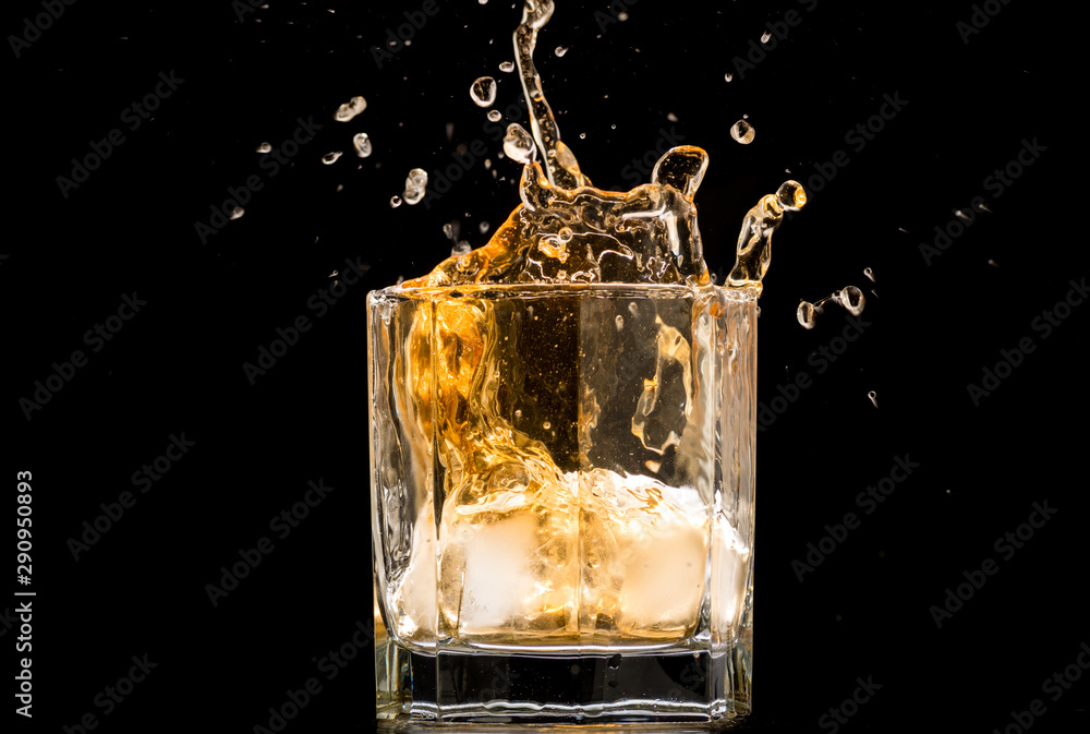 glass of whiskey with ice and a splash and spray from falling on a black background