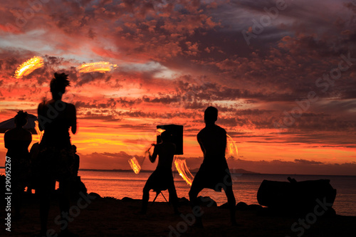 Silhouettes of fire spinners on beach with red sunset sky in Fiji