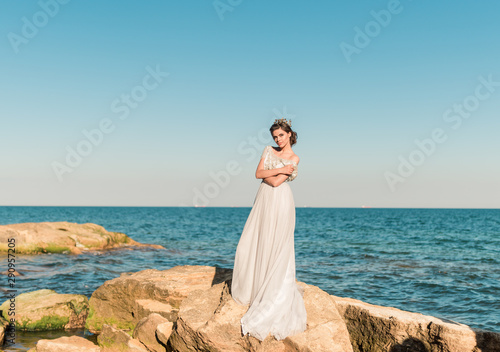 Beautiful bride outdoors . Wedding hairstyle and make up. Romantic beautiful bride in long luxury dress posing on the beach with bouquet of flowers