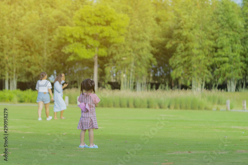 A little girl in a pink skirt enjoys a relaxing time playing on the green lawn at the public park in the evening.