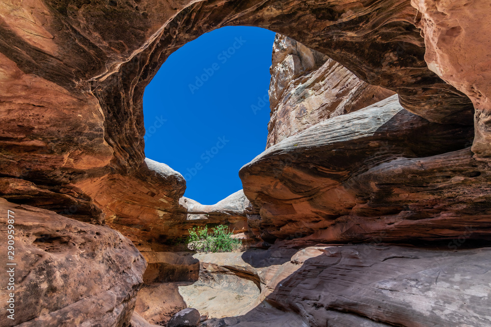 Wide angle view of a natural cave carved into red sandstone under a spotless blue sky