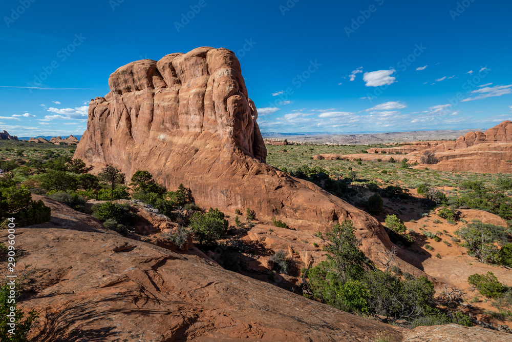 Fototapeta premium Wide angle view of a large red sandstone monolith in Arches National Park, under a blue sky with sparse clouds