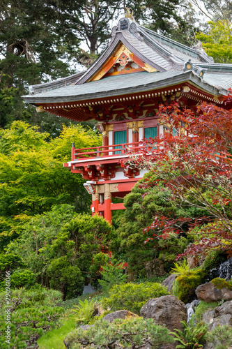 A red japanese pagoda temple surrounded by green vegetation and moss-covered rocks