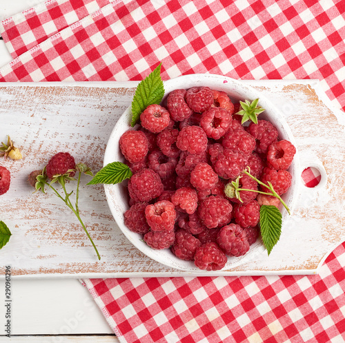 ripe red raspberries in a white wooden plate on a table of boards