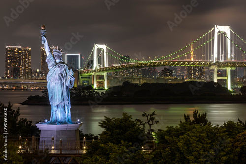 Tokyo skyline at night as seen from Odaiba, with a suspension bridge a statue of liberty replica