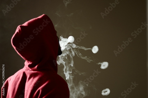 Young male in red hoodie vaping smoking, blows 4 smoke rings, isolated rear view photo