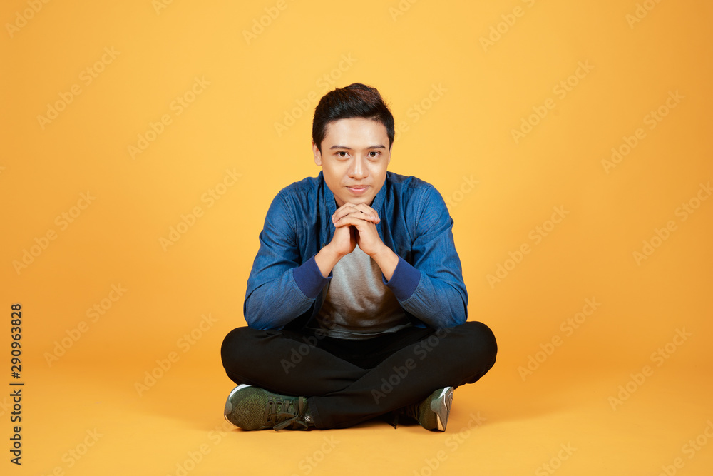 Good looking young Asian man sitting with legs crossed on the floor, isolated on orange background. Good looking young Asian man sitting with legs crossed on the floor, isolated on orange background.