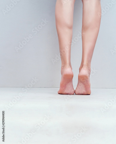 Female slender legs, feet are on the light gray background floor.