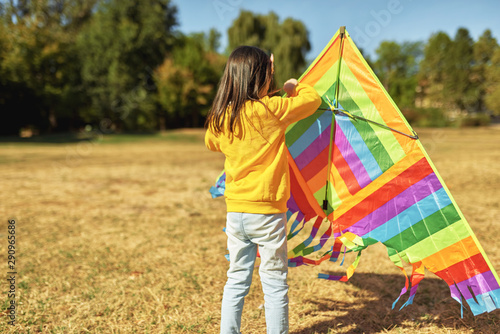 Rear view image of a happy child, little girl launching a colorful kite on a sunny day outdoors. Cute kid playing and have fun outside with a kite in the park.
