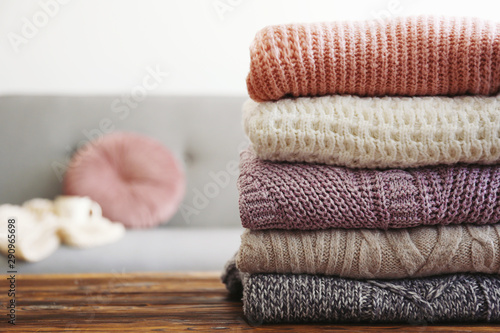 Bunch of knitted pastel color sweaters with different knitting patterns perfectly folded in stack on brown wooden table, white brick wall background. Fall winter season knitwear. Close up, copy space © Evrymmnt