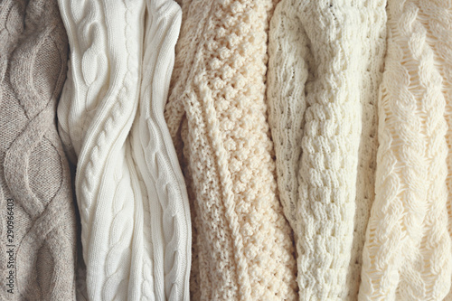 Bunch of knitted warm pastel color sweaters with different vertical knitting patterns hanging in bunch, clearly visible texture. Stylish fall / winter season knitwear clothing. Close up, copy space.