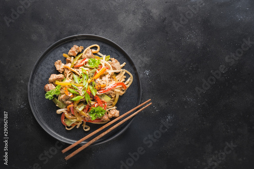 Udon stir-fry noodles with pork bowl and vegetables on black stone background. Asian cuisine. Top view. Copy space.