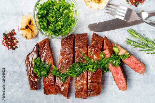 Foto Sliced rib eye beef steak with chimichurri sauce and spices on white paper