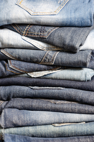A stack of carelessly folded jeans on gray background. Close-up of jeans in different colors. Jeans texture or denim background