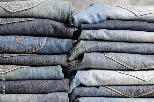 Neatly folded jeans in two piles on a gray background. Close-up of jeans in different colors. Jeans texture or denim background