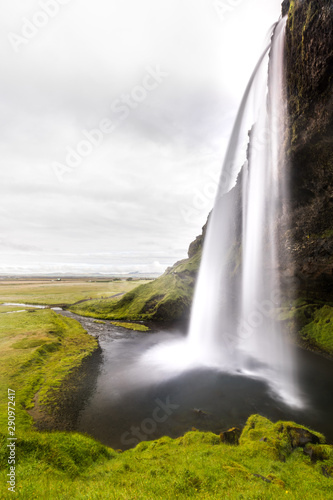 Icelandic landscape with the iconic waterfall of Seljalandsfoss under a cloudy sky