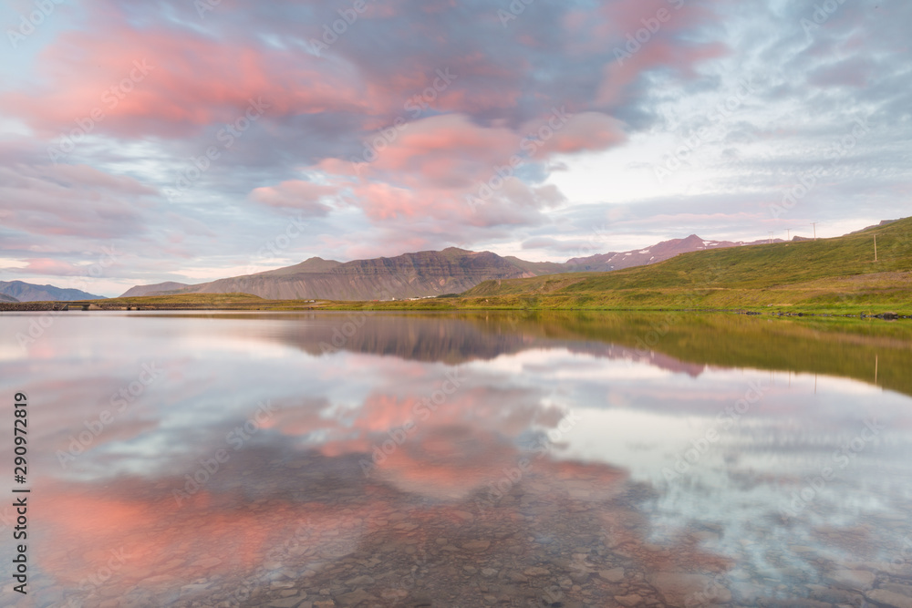 Symmetrical shot of an icelandic landscape, with pink clouds and distant mountains reflecting on a still lake