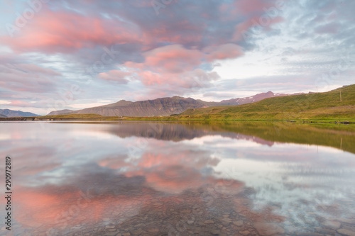 Symmetrical shot of an icelandic landscape  with pink clouds and distant mountains reflecting on a still lake