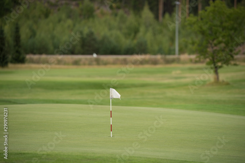 Single white flag marking the holes in golf course. Empty emerald green fields, putting areas. Summer afternoon in central Finland, Scandinavia.