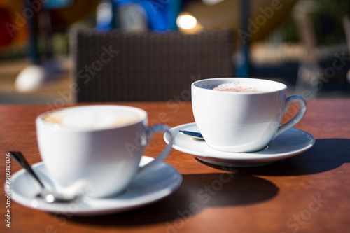 cappuccino, coffee, in two white cup and saucer, on wooden terrace table