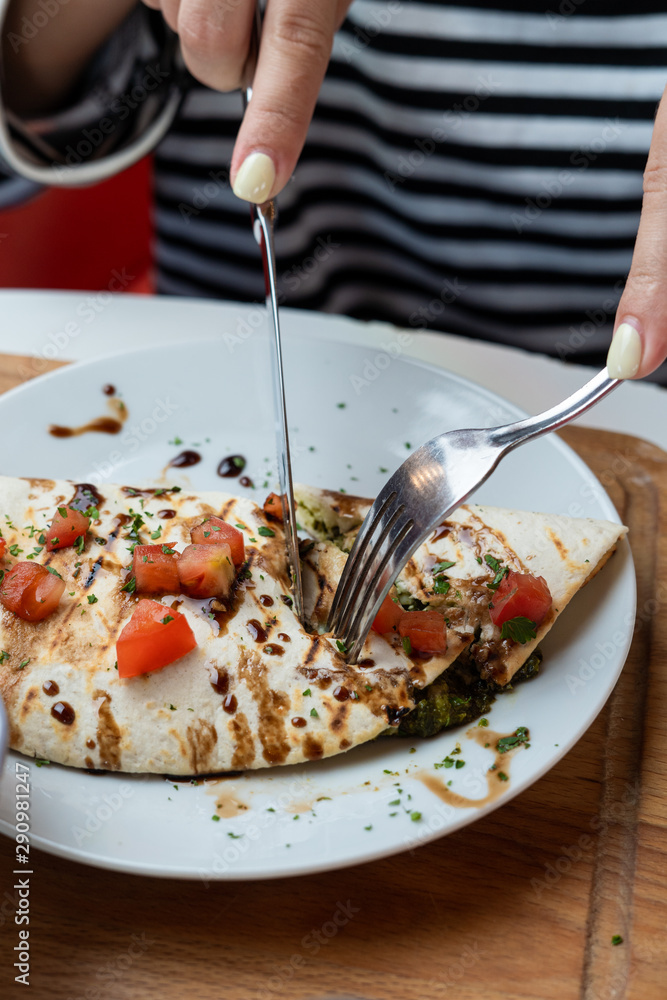 Young european woman is eating mexican quesadilla with knife and fork and cutting it in pieces Young european woman is eating mexican quesadilla with knife and fork and cutting it in pieces