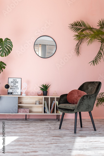 Minimalistic and luxury pastel pink home interior with green velvet design armchair, plants and mirror